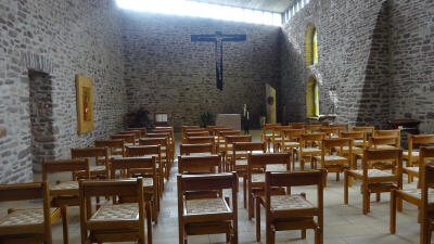 Mehrere handgefertigte Kirchenstühle mit geflochtenen Sitzkissen in einem historischen Kirchenraum aus Bruchsteinmauerwerk